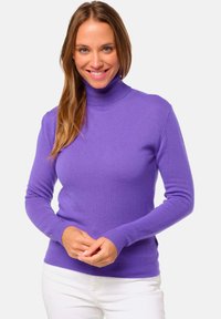 Pull à col roulé violet en tricot doux, avec des manches longues et des poignets côtelés. Porté avec un pantalon blanc, il présente une silhouette ajustée.