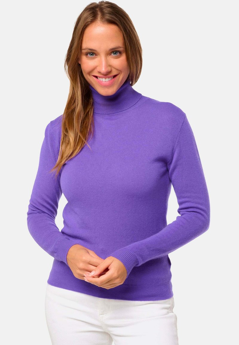 Pull à col roulé violet en tricot doux, avec des manches longues et des poignets côtelés. Porté avec un pantalon blanc, il présente une silhouette ajustée.