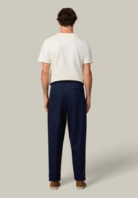 Lichtbeige T-shirt met korte mouwen, gecombineerd met donkere marineblauwe broek. De broek heeft zij- en achterzakken, een gladde textuur en een getailleerde pasvorm.