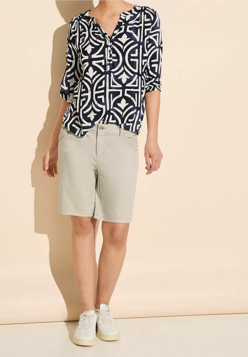 Navy blouse with white abstract pattern, short beige shorts, and white sneakers. Blouse has a V-neck and three-quarter sleeves.