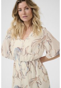 Könnyű, mintás ruha krém színben, lovakkal illusztrálva, V-nyakkal, lebegő ujjakkal és megkötős derékrésszel a formázás érdekében. Texturált szövet.