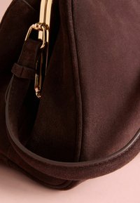 Geanta de mână din suede maro are o textură netedă, o formă rotundă și un închizător și accesorii din metal auriu.