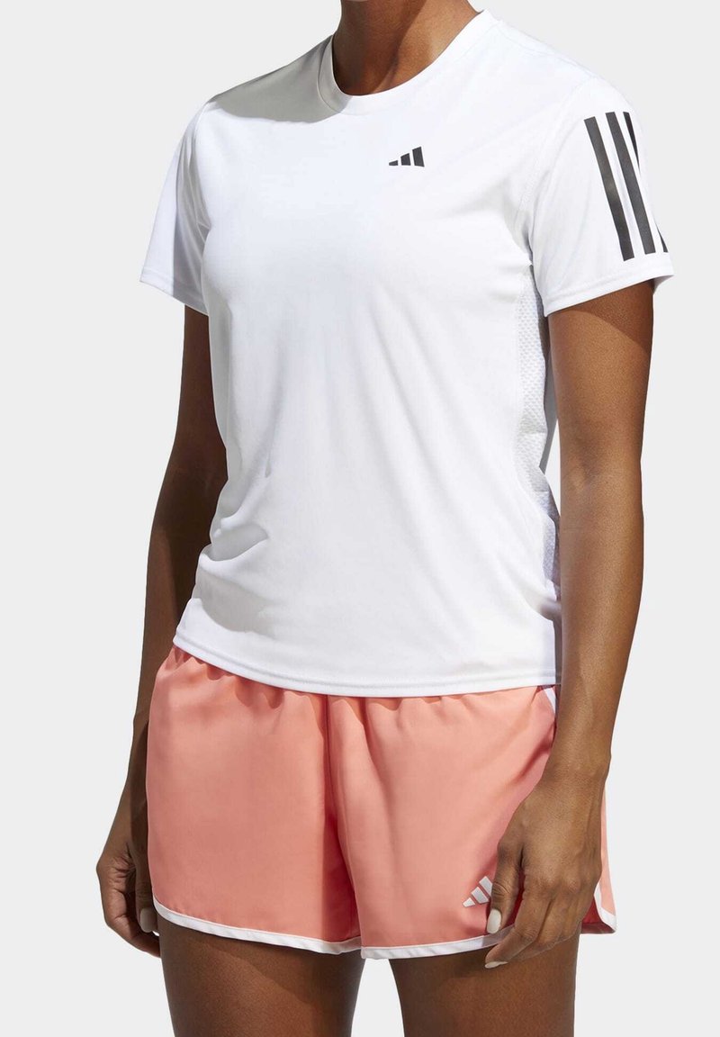 Vit sporttröja med kort ärm, med tre svarta ränder på vänster axel. Matchad med ljusrosa shorts och vita detaljer.