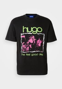 Svart bomullst-skjorte med et grønt "hugo"-logo, et rosa grafisk bilde med bandbilder, og teksten "The feel good dep." i grønt.