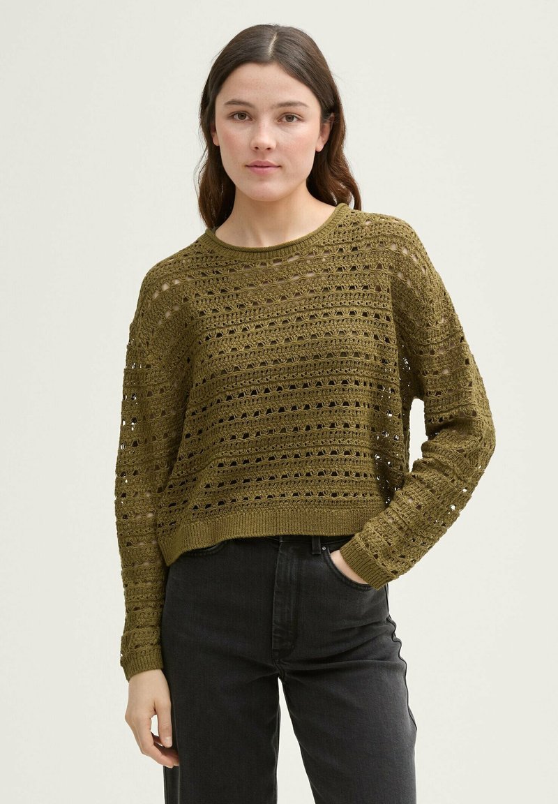 Olijfgroen cropped gebreid sweater met openwork patronen, ronde hals en lange mouwen; gecombineerd met donkere jeans.