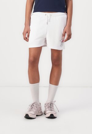 Hvite bomullsshorts med snor i livet, sidelommer og grafisk trykk. Kombinert med mid-lange hvite sokker og lyserosa sko.