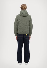 Olive green padded jacket with a hood, featuring a textured surface and a cropped length. Paired with navy blue cargo pants and white shoes.