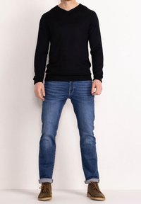 Czarny sweter z dekoltem w serek, dopasowany fason, długie rękawy. Jasnoniebieskie dżinsy, prosty krój, podwinięte na kostkach. Brązowe skórzane botki.
