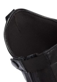 Soporte para tobillo negro con un forro interior texturizado, que cuenta con un cierre metálico a presión y una correa elástica para un ajuste seguro.
