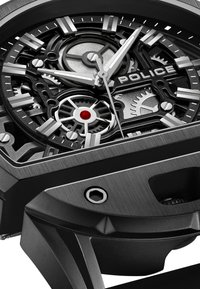 Czarny zegarek ze stali nierdzewnej z odsłoniętym cyferblatem, srebrnymi znacznikami godzinowymi i czerwonymi akcentami. Posiada wyrazisty, kanciasty kształt koperty oraz odsłonięte mechanizmy.