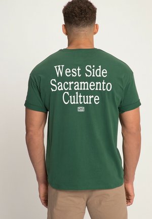 Grøn bomulds T-shirt med hvid tekst på ryggen, der står "West Side Sacramento Culture". Kortærmet og med rund hals.