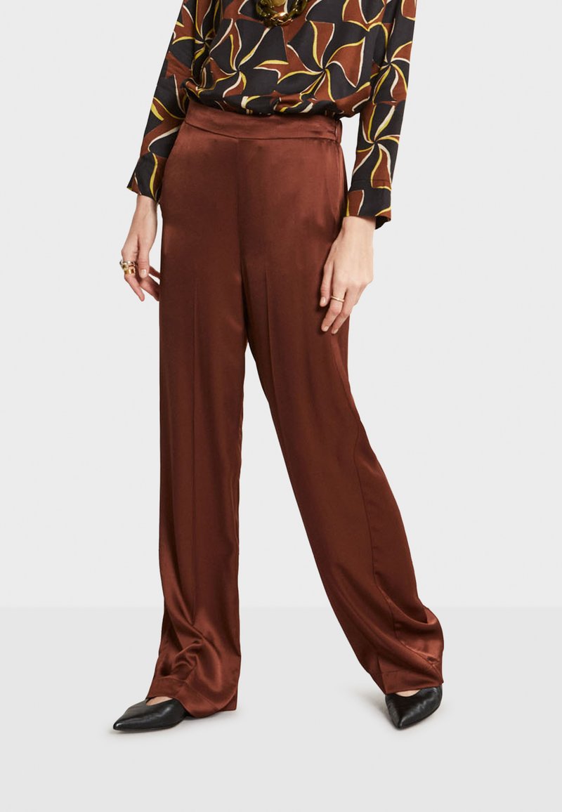Pantalons larges en satin marron avec une texture lisse, dotés d'une taille haute et d'un léger brillant, associés à des chaussures noires à bout pointu.