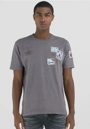 Camiseta de algodón gris con mangas cortas, cuello redondo y varios estampados impresos en detalles azules, rosas y marrones. Dobladillo desgastado en las mangas.