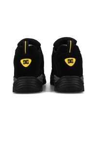 Černé semišové sportovní boty s šedou gumovou podrážkou, vybavené žlutým logem DC na zadní straně a černožlutým poutkem. Zaoblený design, polstrované.