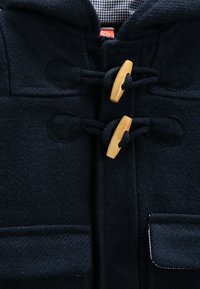 Granatowy wełniany płaszcz typu duffle z kapturem, dużymi przednimi kieszeniami, drewnianymi zapięciami na toggles oraz czarną bawełnianą podszewką w kratkę.