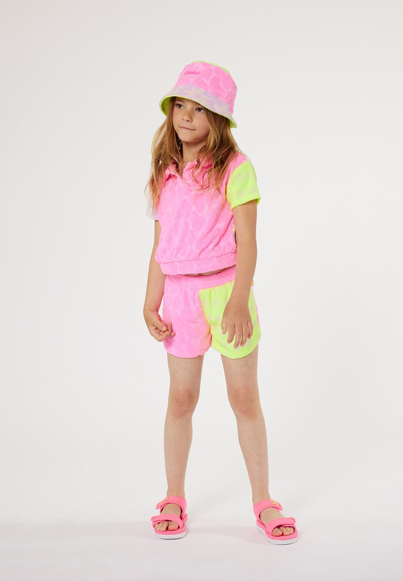 Ensemble en tissu éponge rose vif avec des accents jaunes fluo. Comprend un haut à manches courtes, un short et un chapeau seau assorti. Des sandales roses complètent le look.