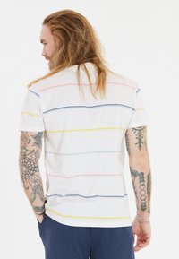 Valkoinen lyhythihainen T-paita, jossa on vaakasuoria raitoja vaaleanpunaisessa, vihreässä, keltaisessa ja sinisessä. Puuvillamateriaali ja rento malli.