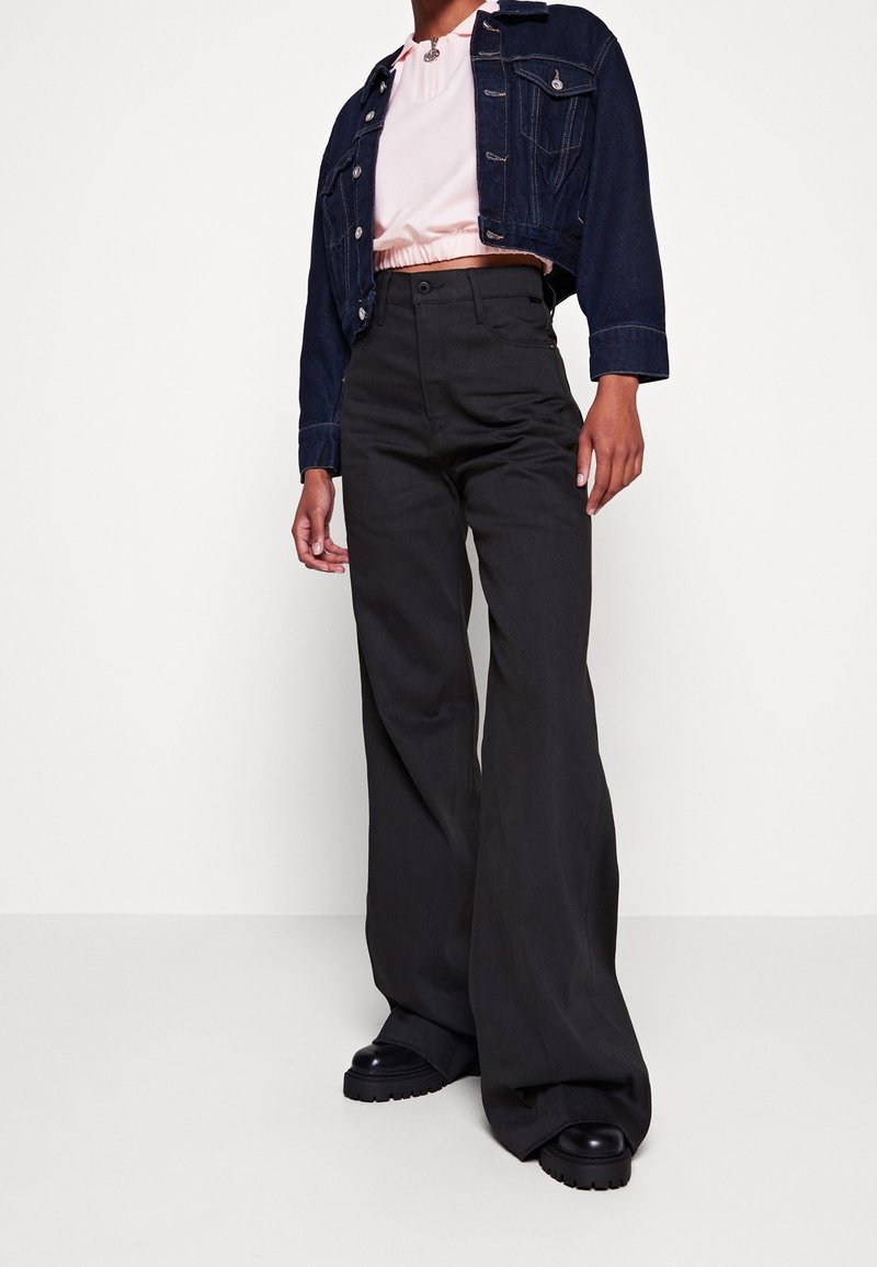Pantalones de pierna ancha en gris oscuro combinados con un top rosa corto y una chaqueta de mezclilla oscura ajustada, con un diseño clásico y detalles de botones.