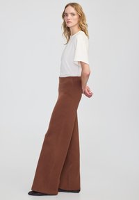 Bruine wijde broek met een gladde textuur, hoge taille en een losse pasvorm. Gepaard met een lichtgekleurde, korte mouw top. Eenvoudig ontwerp.