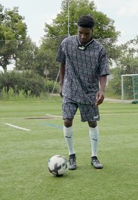 Svart och vit mönstrad fotbollsdräkt i lättviktigt tyg, med en lös skjorta och shorts. Vita knähöga strumpor och svarta fotbollsskor.