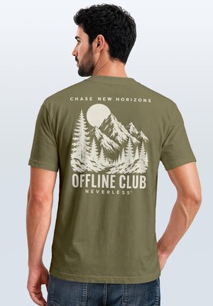 Mann trägt ein olivgrünes T-Shirt mit Berg-, Baum-, Mond-Grafik und Text "Chase New Horizons Offline Club Neverless" auf dem Rücken.