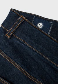 Mörkblå denimjeans med synlig sömnad i en kontrasterande orange färg, med knappstängning och bältesöglor i midjan.