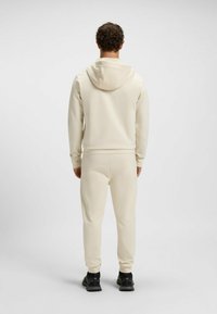Ljusbeige hoodie och matchande joggers i slätt tyg. Funktioner inkluderar en huva, åtsittande mudd och sidofickor. Enkel, minimalistisk design.