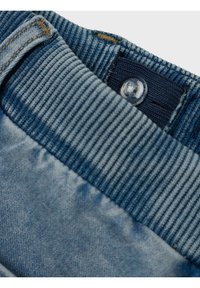 Cintura in denim con texture a coste di colore blu scuro. Tessuto in denim di colore blu chiaro con un leggero sbiadimento e un chiaro dettaglio del bottone.