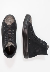 Černé vysoké tenisky vyrobené z nubuku s texturovanou, tečkovanou špičkou. Disponují černými tkaničkami, gumovou podrážkou a kulatým logem na boku.