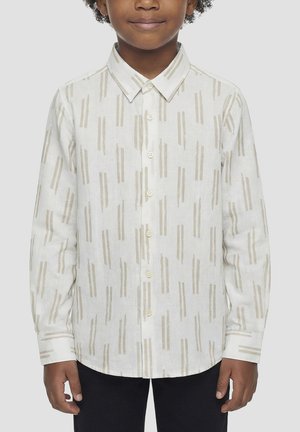 Bambino che indossa una camicia bianca con bottoni e motivi a righe verticali beige, in piedi con le mani rilassate lungo i fianchi.