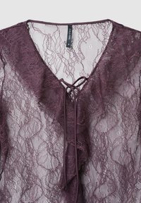 Top in pizzo color malva scuro con scollo a V, bordi arricciati e chiusura annodata. Presenta motivi floreali intricati e una texture leggera e trasparente.