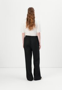 Black wide-leg trousers with an elastic waistband, paired with a white short-sleeve blouse, viewed from the back. Smooth texture.