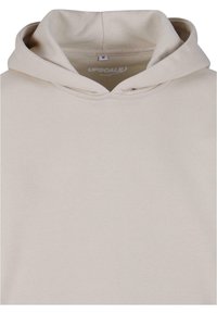Beige hoodie med snoretræk i hætten og ribstrikkede manchetter. Fremstillet af blødt stof, med et mærke indeni der viser brandnavnet "UPSCALE" og størrelse "M."