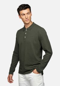 Polo a maniche lunghe di colore verde scuro in cotone, con colletto, pattina con tre bottoni e un logo discreto sul petto.