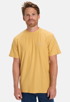 Korte mouwen, ronde hals t-shirt in mosterdgeel, gemaakt van een gestructureerde stof, met een klein logo op de borst. Gecombineerd met blauwe jeans.