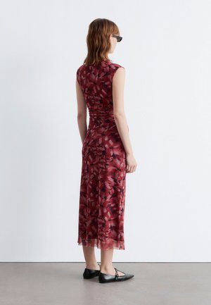 Rotes Midi-Kleid mit floralem Muster, kurzen Ärmeln, tailliertem Oberteil und fließendem Rock. Getragen mit schwarzen flachen Schuhen, von hinten betrachtet.