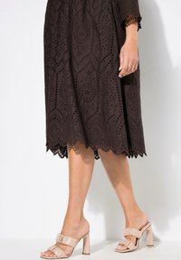 Braunes besticktes Kleid mit Laserschnittmustern, gewelltem Saum, kombiniert mit nuden Blockabsatzsandalen mit einem frilligen Riemen.