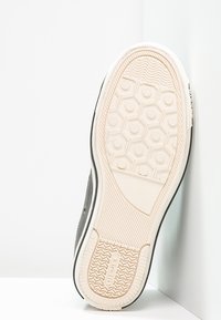 Czarna podeszwa trampka z wzorzystym gumowym spodem, featuring heksagonalne kształty, teksturowane akcenty oraz białą ścianę boczną.