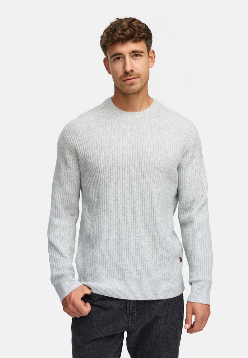 Maglione lavorato a maglia di un grigio chiaro con una texture a costine, scollatura rotonda e maniche lunghe. Presenta una piccola etichetta con logo sull'orlo. Indossato con jeans scuri.