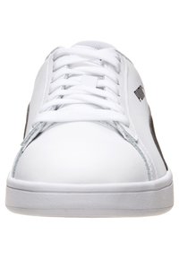 Zapatilla de cuero blanca con puntera redondeada, que presenta acentos grises en los laterales y una suela de goma texturizada. Los cordones son centrales y planos.