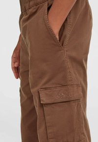 Pantaloni cargo marroni realizzati in tessuto resistente, dotati di tasche laterali e un logo ricamato sulla patta della tasca superiore. Vita elastica.