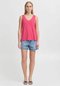 Ružový v-neck top bez rukávov v kombinácii so svetlomodrými džínsovými šortkami. Top je vyrobený z mäkkého materiálu s voľným strihom, zatiaľ čo šortky majú klasický strih.
