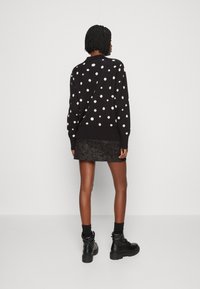 Un pull noir avec des pois blancs, encolure ronde, manches côtelées, associé à une jupe noire texturée. Le modèle porte des bottes noires et des chaussettes.