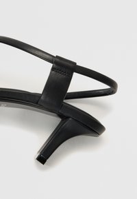 Sandale negre din piele cu toc înalt, cu un design cu curea îngustă. Dispune de un vârf ascuțit și un toc geometric pentru stabilitate.