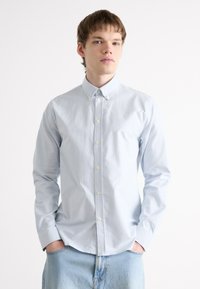 Chemise boutonnée bleu clair avec des rayures verticales blanches ; dotée d'un col classique, de manches longues et d'une coupe ajustée. Matière en coton doux.