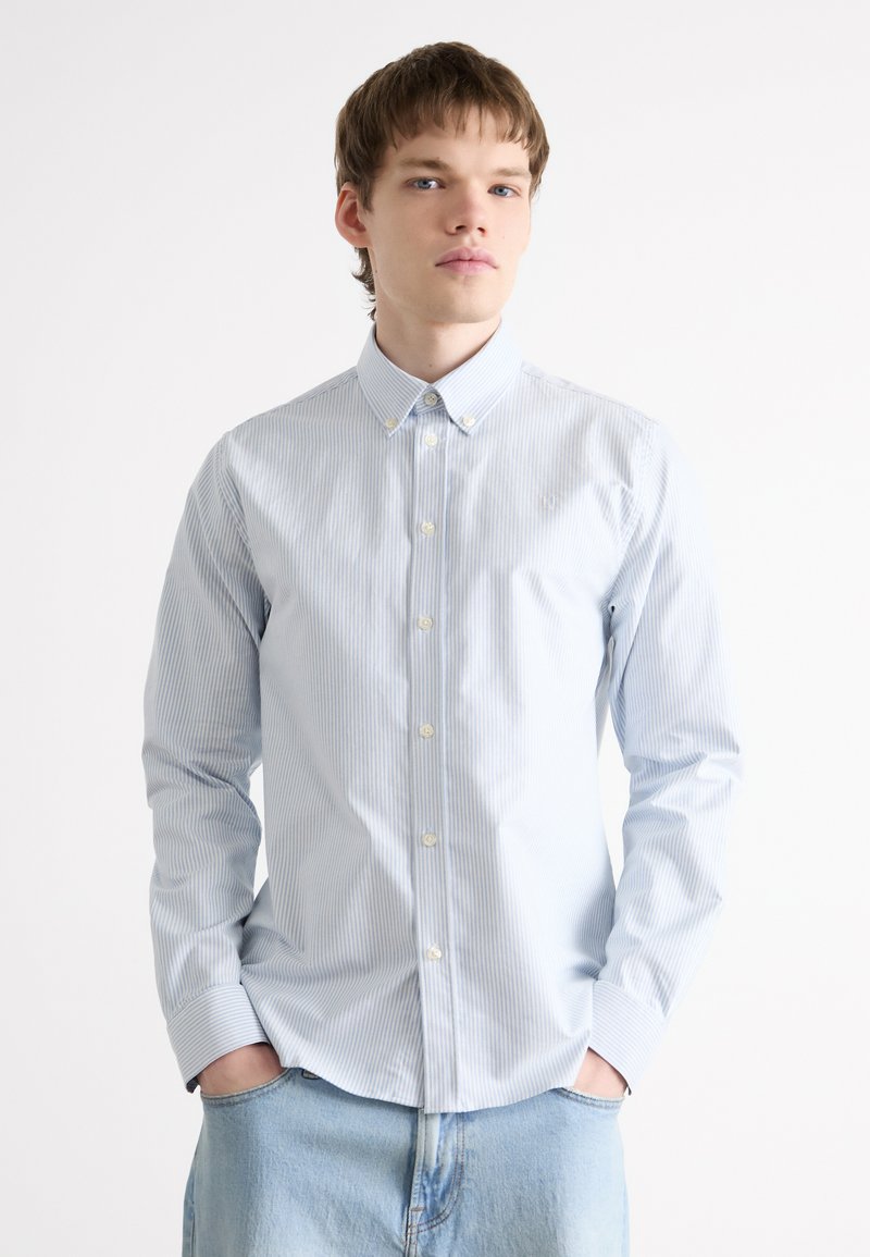 Chemise boutonnée bleu clair avec des rayures verticales blanches ; dotée d'un col classique, de manches longues et d'une coupe ajustée. Matière en coton doux.