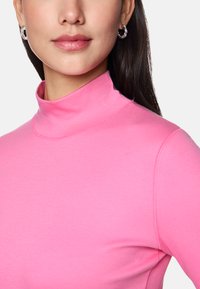 Fitted, high-neck top in bright pink, made from smooth, stretchy fabric. Features subtle seam detailing and a lightweight texture.