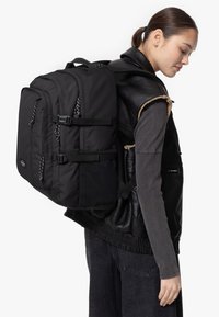 Sac à dos noir avec plusieurs compartiments, bandoulières réglables et finition texturée. Comprend des poches latérales et des détails de fermeture éclair contrastants.