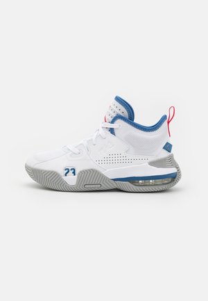 Chaussure de basketball montante blanche avec des accents bleus et rouges, une semelle à coussin d'air visible, et le numéro 23 sur le côté.