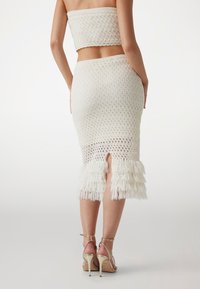 Ensemble en crochet blanc composé d'un haut sans bretelles et d'une jupe longueur genoux avec un ourlet à franges et une fente à l'arrière. Matière texturée.